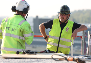Tvä byggnadsarbetare står och pratar iklädda arbetskläder