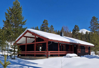 Stuga med snö och skog i bakgrunden.
