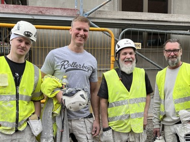 Byggnads medlemmar står uppradade på bild framför ett bygge.