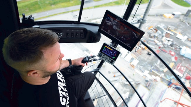 Kranförare ser ner från hytt på arbetsplatsen