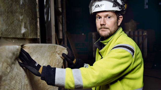 Byggnadsarbetare arbetar med isolering på huk i mörkt rum