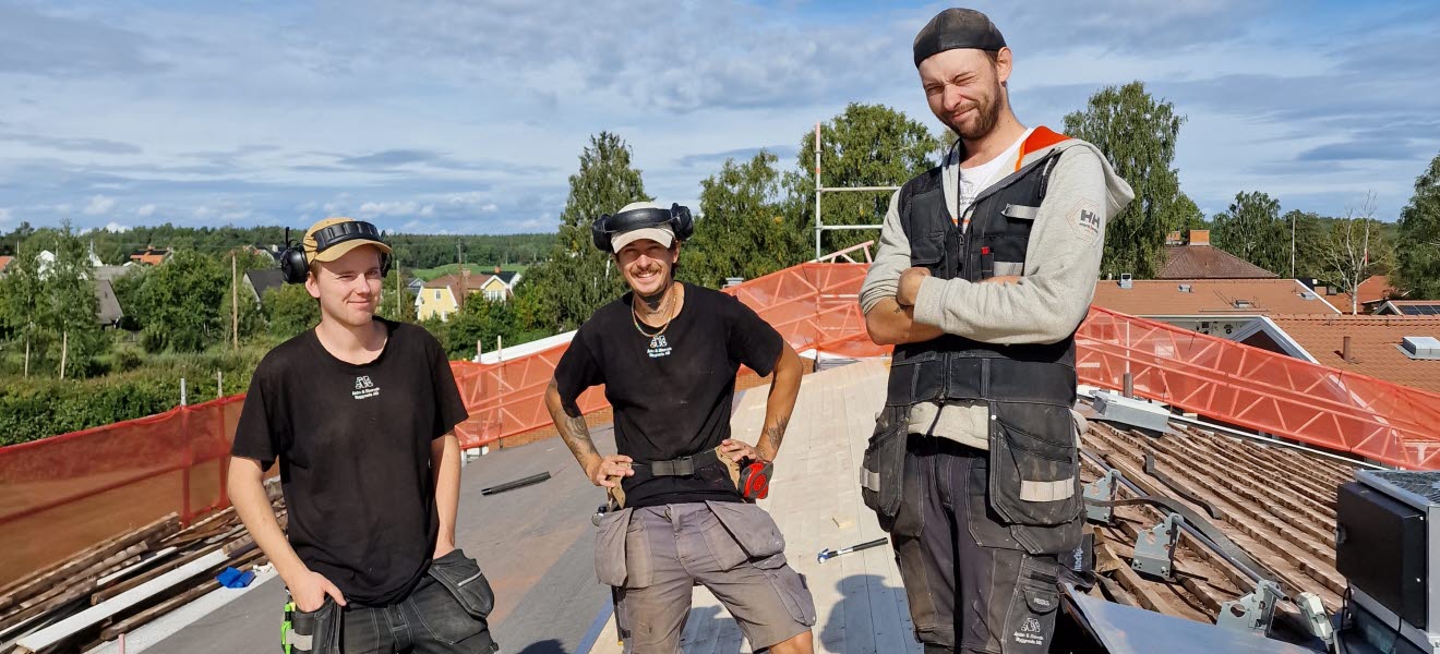 Tre medlemmar poserar för bild på ett tak