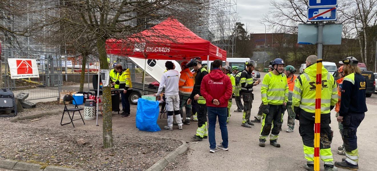 Byggnads Öst står och grillar korv i Byggnadstältet. Byggnadsarbetare står i kö för korv och facklig information.