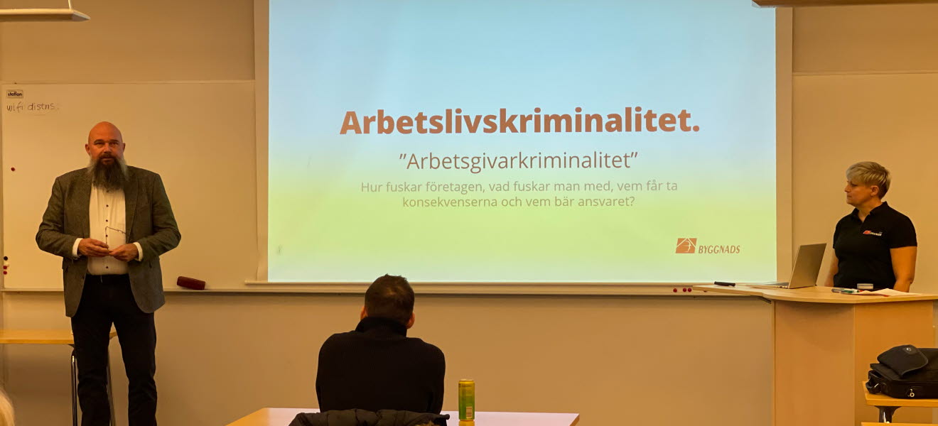 Två föreläsare och ryggen av en i publiken. På tavlan står det Arbetslivskriminalitet "Arbetsgivarkriminalitet"