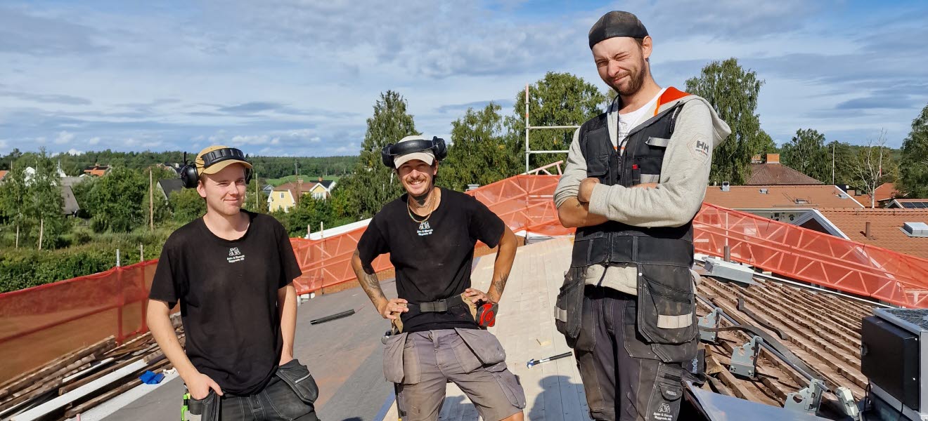 Tre byggnadsarbetare står och poserar på ett tak